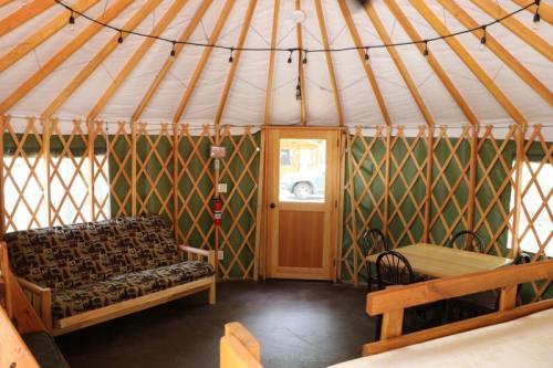 Interior of a yurt featuring a wooden frame, a sofa, a dining table, and string lights.