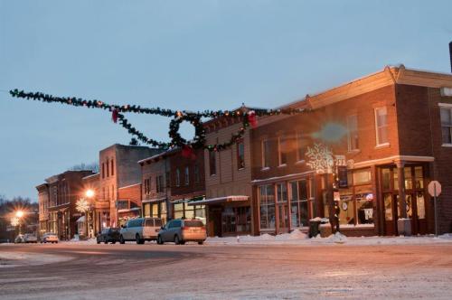 A snowy street scene with decorated buildings and festive garlands overhead, creating a cozy holiday atmosphere.