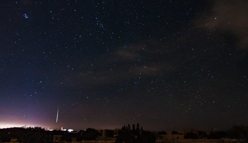 A starry night sky with a bright meteor streaking across, illuminating the landscape below.