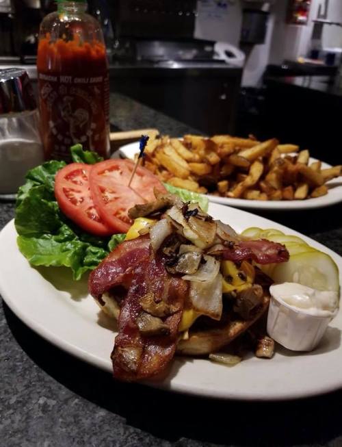 A delicious burger topped with bacon, cheese, onions, and pickles, served with lettuce, tomato, and a side of fries.