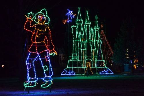 Colorful holiday lights depict a whimsical figure and a castle against a dark night sky.