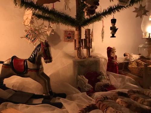 A cozy holiday scene featuring a wooden rocking horse, dolls, and festive decorations under a softly lit tree.