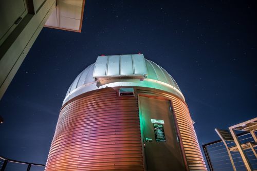 A wooden observatory dome under a starry night sky, illuminated with colorful lights.