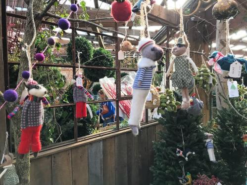 Colorful handmade animal decorations hang in a greenhouse, surrounded by greenery and festive ornaments.