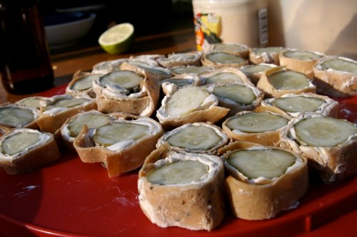 A red platter filled with sliced rolls of cream cheese and pickles, showcasing a unique appetizer.
