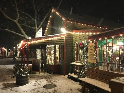 A cozy shop decorated with lights and wreaths, surrounded by snow, creating a festive winter atmosphere at night.