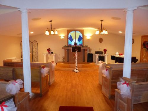 A decorated chapel interior with wooden pews, a stained glass window, and floral arrangements for a wedding.