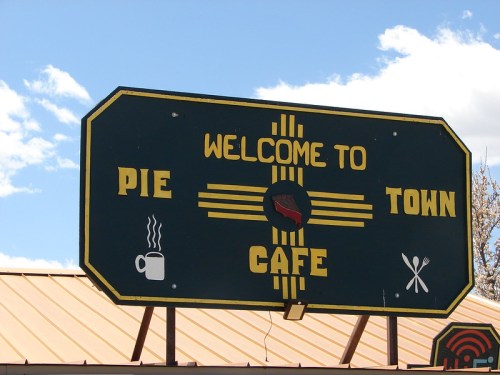 Sign for "Welcome to Pie Town Cafe" featuring coffee and pie icons against a blue sky.