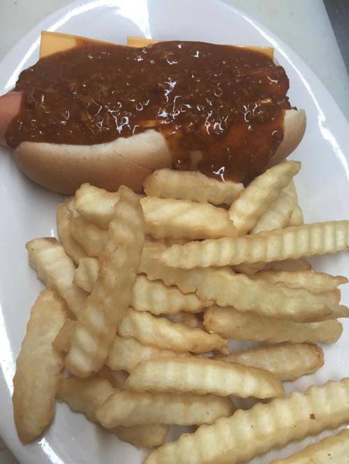 A plate with a chili cheese hot dog and a side of crinkle-cut fries.
