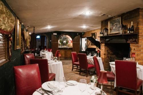 Cozy restaurant interior with red leather chairs, white tablecloths, and a fireplace, featuring elegant decor and dim lighting.