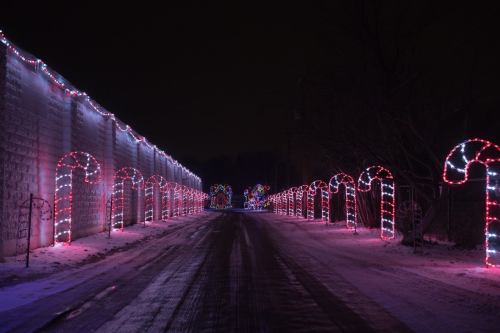 A snowy road lined with colorful candy cane lights and festive decorations on either side.