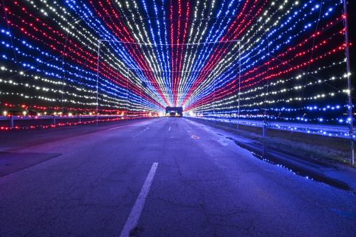 A road illuminated by vibrant red, white, and blue lights creating a tunnel effect at night.