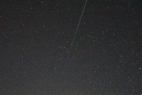 A starry night sky with numerous stars and a bright green meteor streaking across the scene.