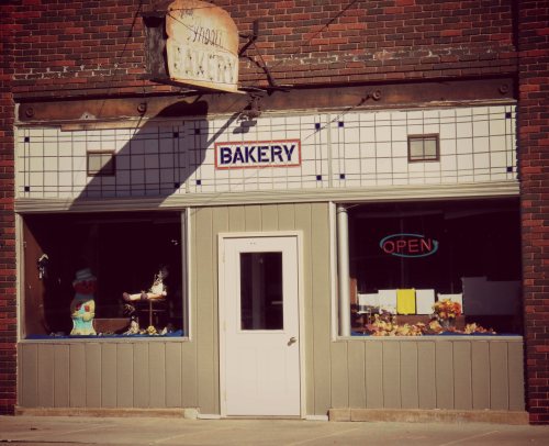 A quaint bakery storefront with a sign reading "BAKERY" and an "OPEN" neon sign, featuring decorative window displays.