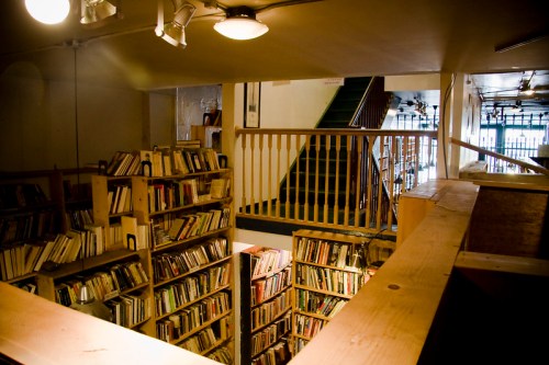 A cozy bookstore with wooden shelves filled with books, overlooking a staircase leading to an upper level.
