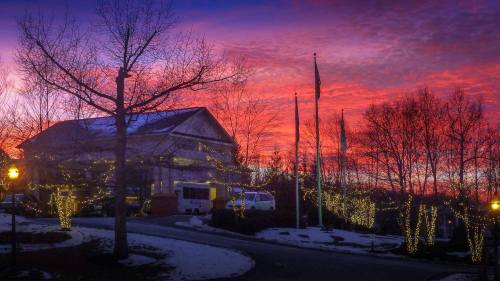 A cozy building adorned with holiday lights, set against a vibrant sunset sky with trees and flags in the foreground.