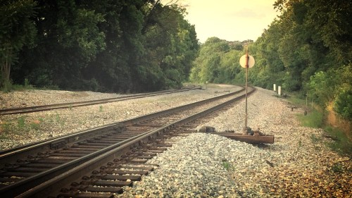 A view of a railway track curving through a green landscape, with a signal post in the foreground.