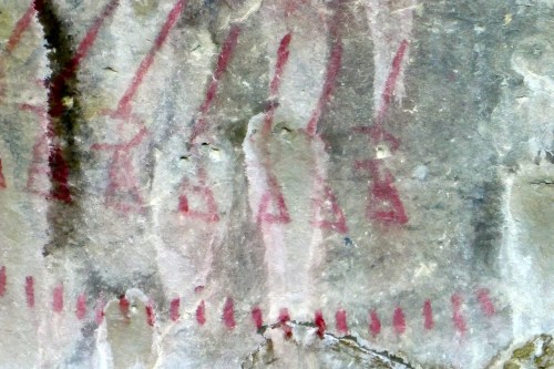 Ancient rock art featuring red figures and symbols on a textured stone surface.