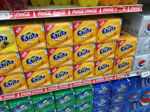 Shelves stocked with Fanta Mango boxes, alongside various soda brands like Coca-Cola and Pepsi.