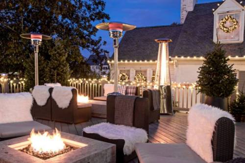 Cozy rooftop lounge with heated seating, a fire pit, and festive holiday decorations under a twilight sky.