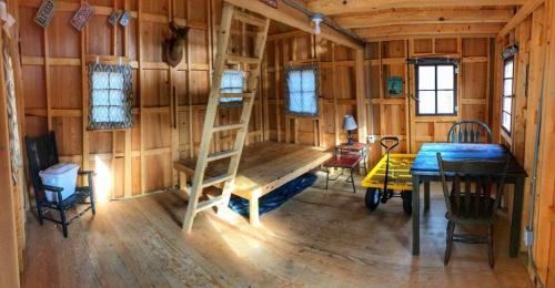 Cozy wooden interior of a cabin featuring a loft bed, table, chairs, and large windows. Warm, rustic atmosphere.