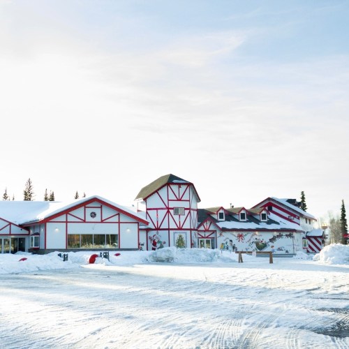 A snowy landscape featuring a festive red and white building with a barn-like design and holiday decorations.