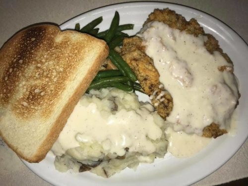 A plate of fried chicken with gravy, mashed potatoes, green beans, and a slice of toasted bread.