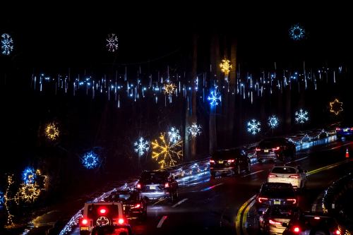 Cars drive along a road adorned with colorful snowflake lights against a dark night sky.