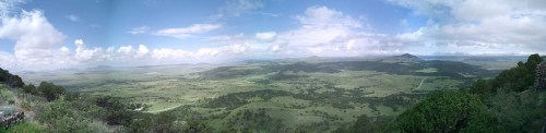 A panoramic view of a lush green landscape under a partly cloudy sky, with distant mountains on the horizon.