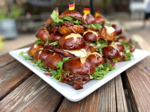 A large platter of stacked pretzel sandwiches filled with greens and meats, garnished with small flags.
