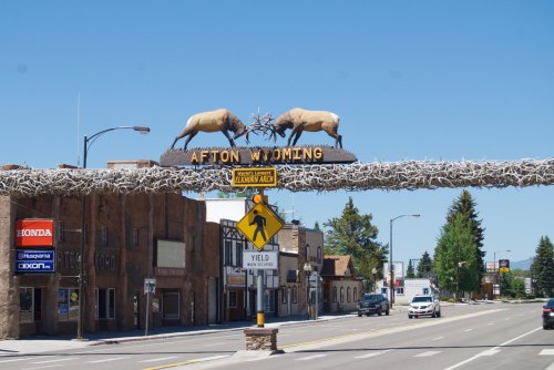 Afton, Wyoming welcome sign featuring two elk antlers atop a wooden arch over a street with shops and trees.
