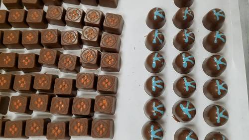 A variety of chocolate candies arranged in rows, featuring floral designs and blue decorations on some.