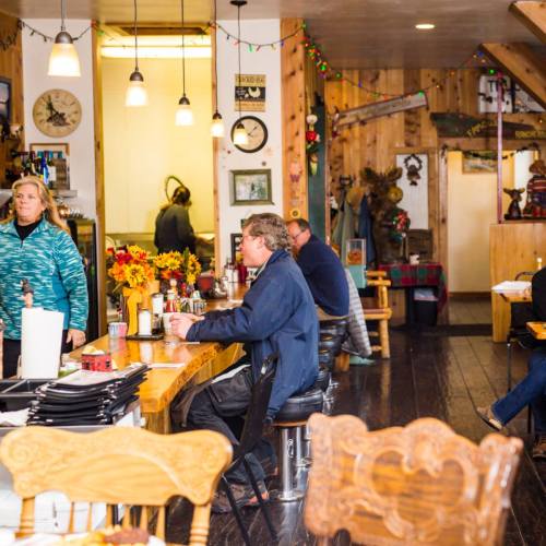 A cozy restaurant interior with wooden decor, patrons at the counter, and a staff member preparing food in the background.
