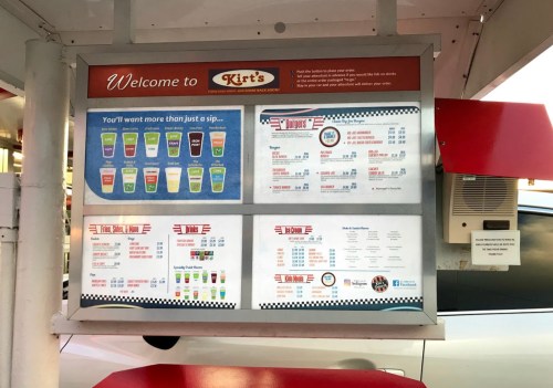 Menu board at Kirt's featuring drinks, burgers, and other food items with prices listed.