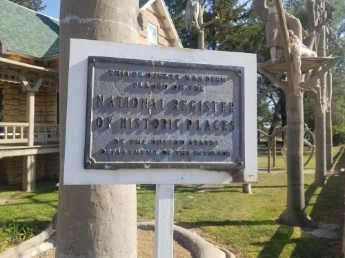 Sign indicating the property is listed on the National Register of Historic Places, with a historic building in the background.