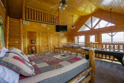 Cozy wooden cabin interior featuring a bed, pool table, and large windows with scenic views.