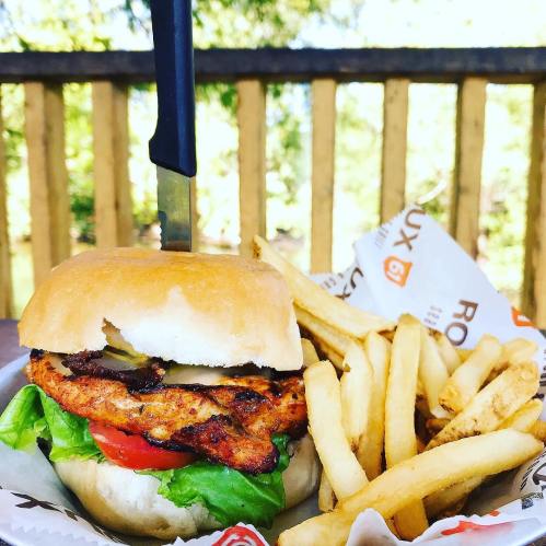 A grilled chicken burger with lettuce, tomato, and pickles, served with a side of golden fries on a wooden table.