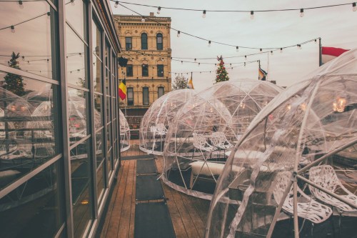 Outdoor dining area with transparent igloo-like structures, string lights, and a historic building in the background.