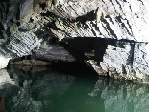 A dark cave interior with rocky walls reflected in still water.