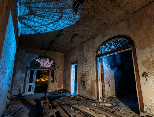 Abandoned room with peeling walls, broken floorboards, and blue lighting illuminating the dark corners.