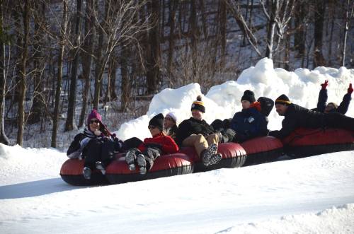 A group of people enjoying snow tubing on a snowy hill, smiling and having fun together.
