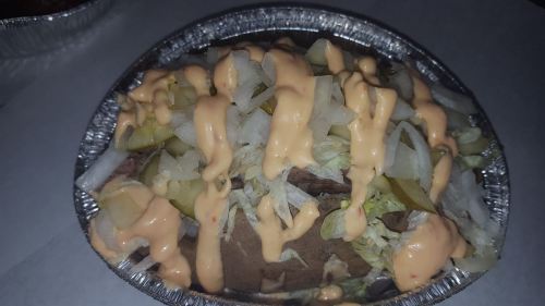 A close-up of a foil container filled with meat, lettuce, onions, pickles, and a creamy sauce on top.