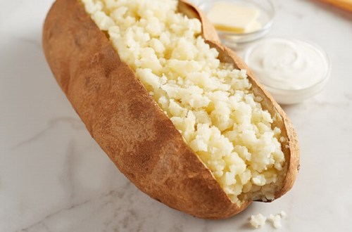 A baked potato split open, filled with fluffy mashed potato, accompanied by butter and sour cream in small bowls.