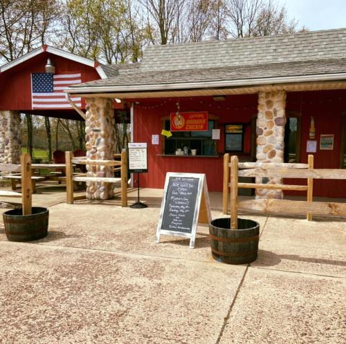 A red building with stone accents, featuring a menu board and an American flag, surrounded by wooden fences and planters.