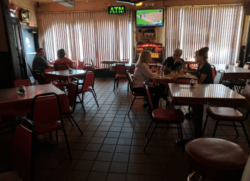 A quiet restaurant interior with red chairs, tables, and patrons enjoying meals, plus a TV showing a sports game.