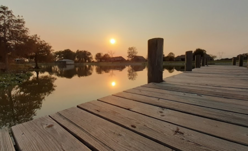 A serene sunset over a calm lake, viewed from a wooden dock with reflections on the water.