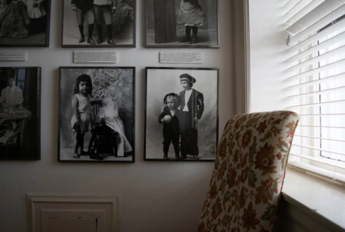 A corner of a room with vintage black-and-white photos on the wall and a floral-patterned chair by a window.