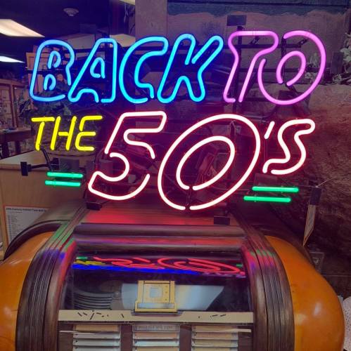 Neon sign reading "Back to the 50's" above a vintage jukebox, evoking a retro diner atmosphere.