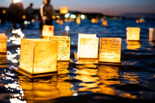 Floating lanterns with handwritten messages illuminate the water at dusk, creating a serene and reflective atmosphere.