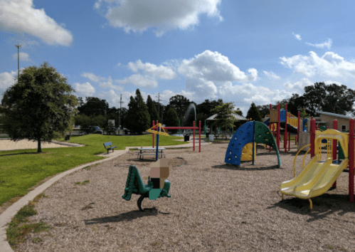 A sunny playground with colorful equipment, including slides, climbing structures, and a sandbox.